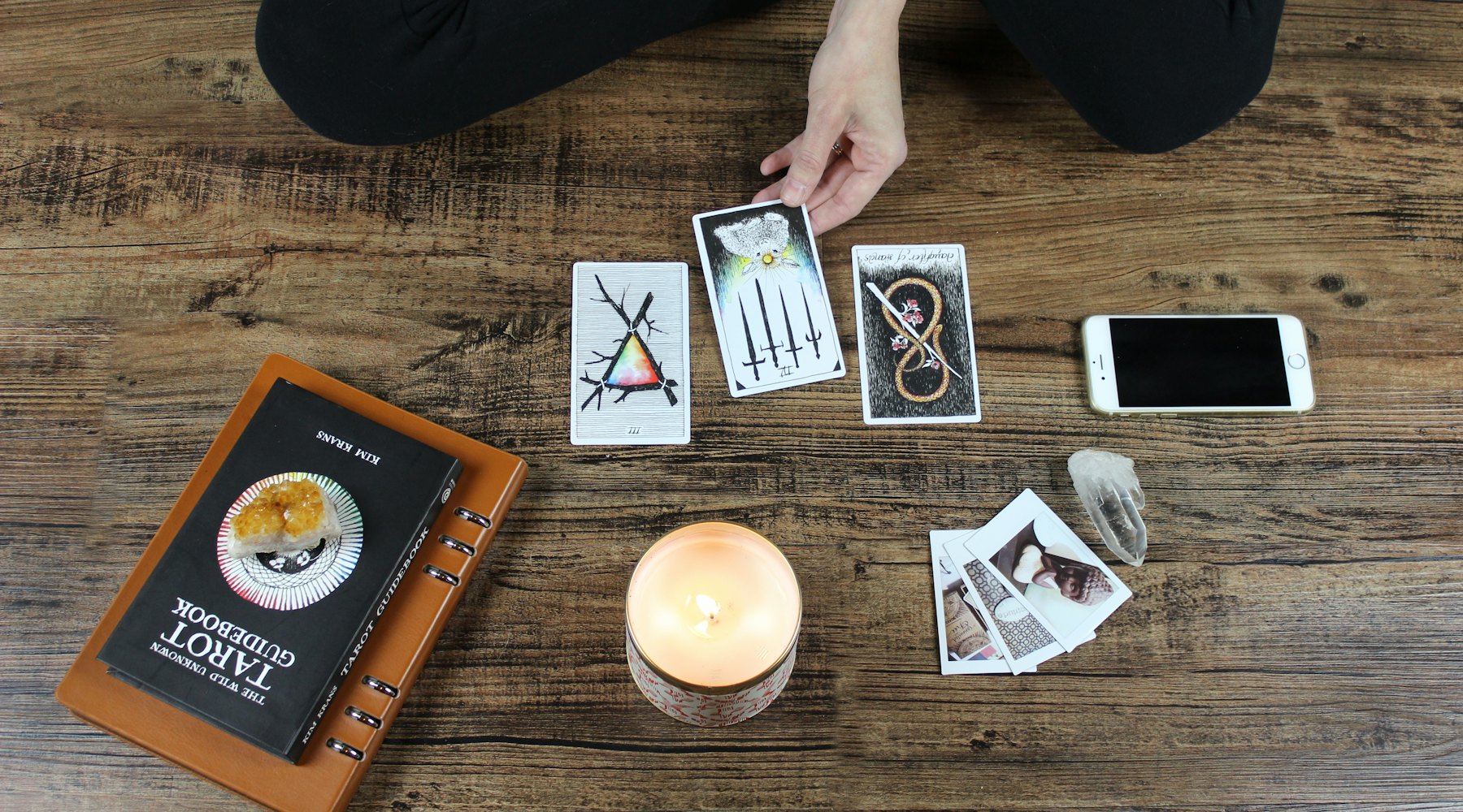 Cartas de tarot, una vela encendida y un cuarzo sobre una mesa de madera